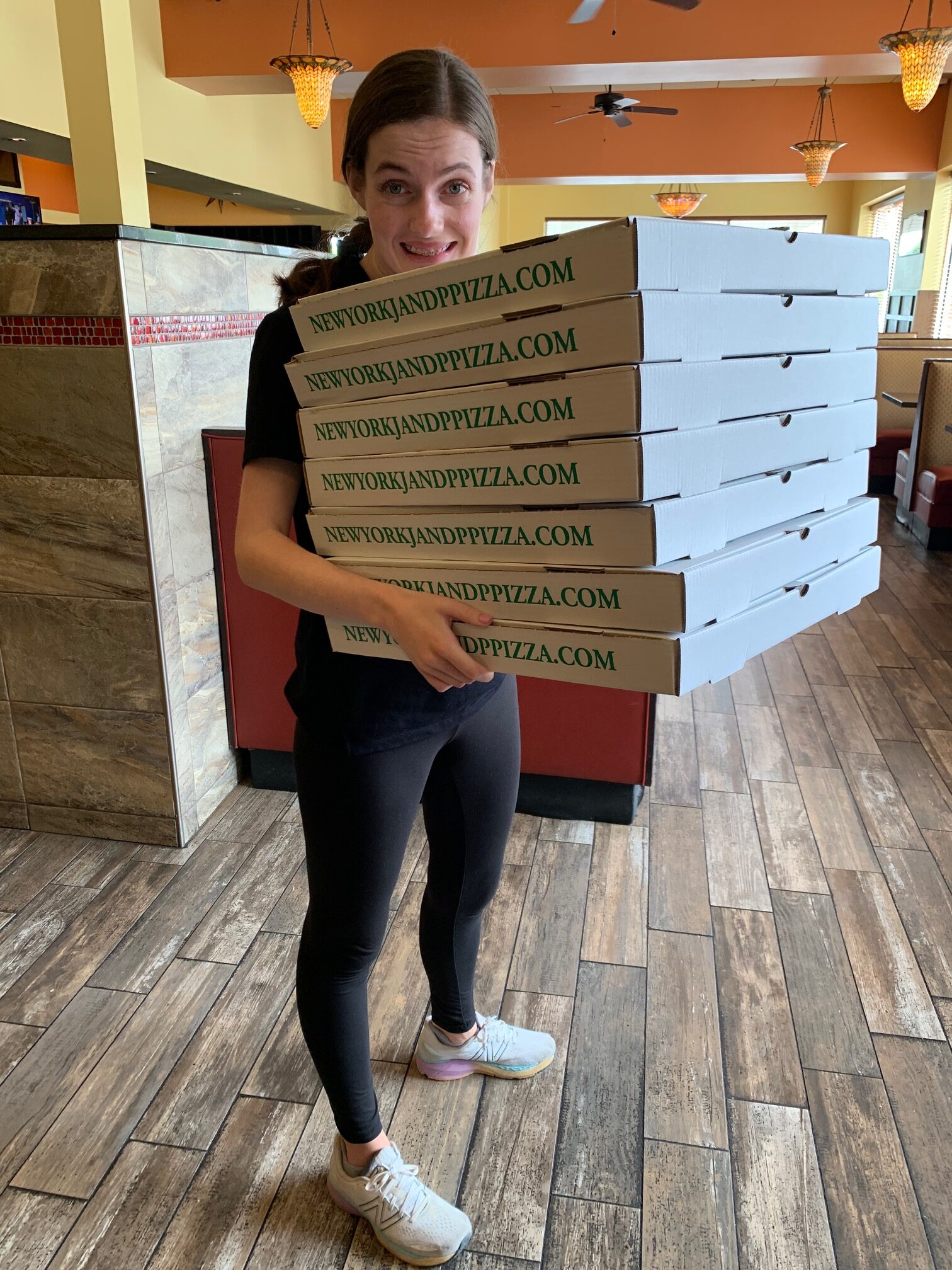 girl stands holding stack of pizza boxes