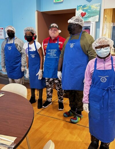 group photo of several people standing in hair nets, blue aprons, and face masks