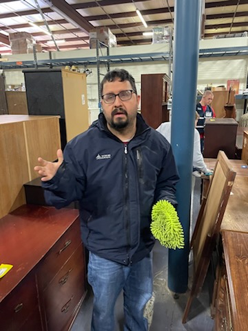 man holding a cleaning rag standing in front of a piece of furniture