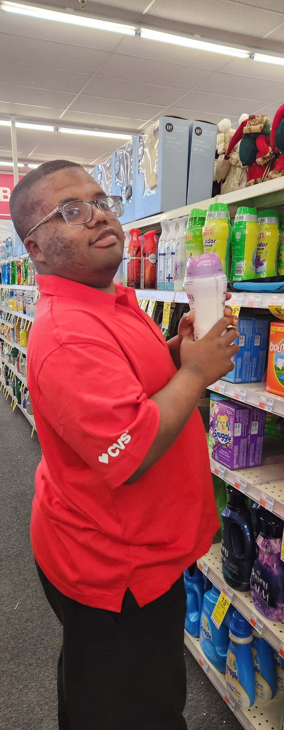 young man with glasses and red shirt holding bottle next to shelf